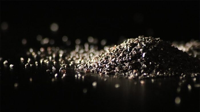 Image is of a pile of Macrogrit Brown Aluminum Oxide abrasive on a black backdrop.
