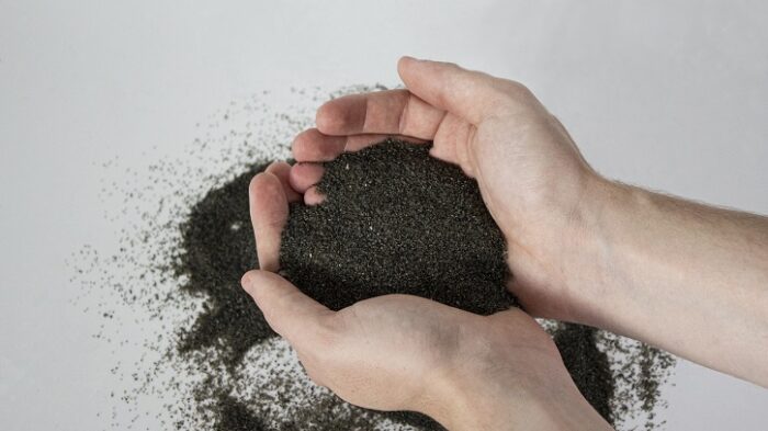 Image is of a pair of hands holding a pile of 10X Abrasives. The abrasives are a dark gray.