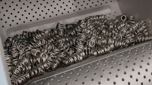 Image is of the interior of a tumble wheel blast machine compartment with just blasted metallic springs resting inside.